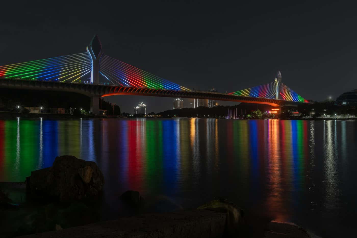 Durgam Cheruvu cable bridge in Hyderabad lit in rainbow colours at night, reflected in the lake
