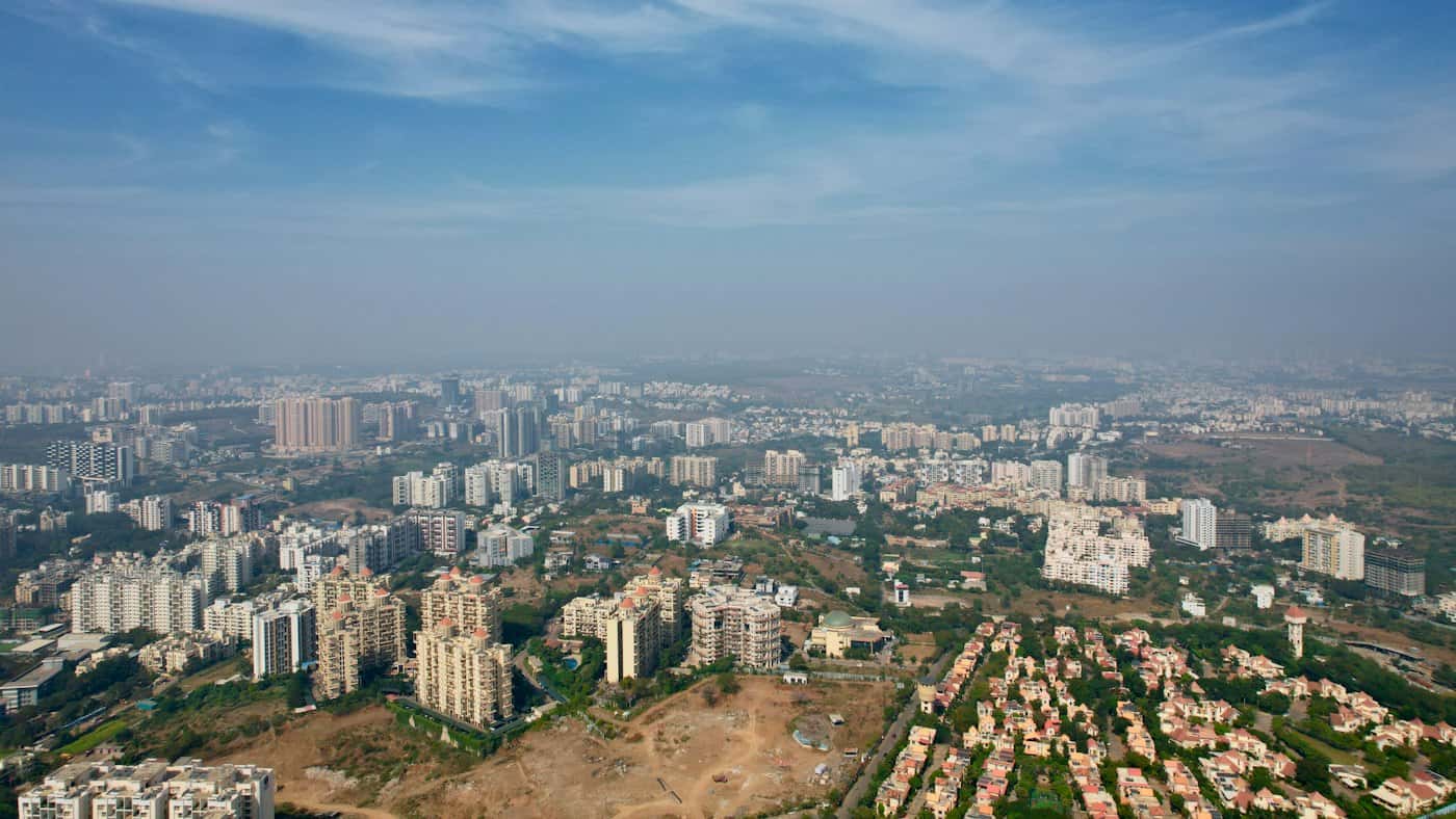 Aerial view over Pune's southern suburbs: apartment towers, villa clusters and open land in hazy daylight