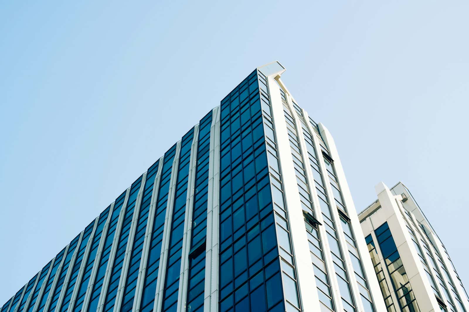 Low-angle view of a blue glass office tower with white vertical fins against a clear sky