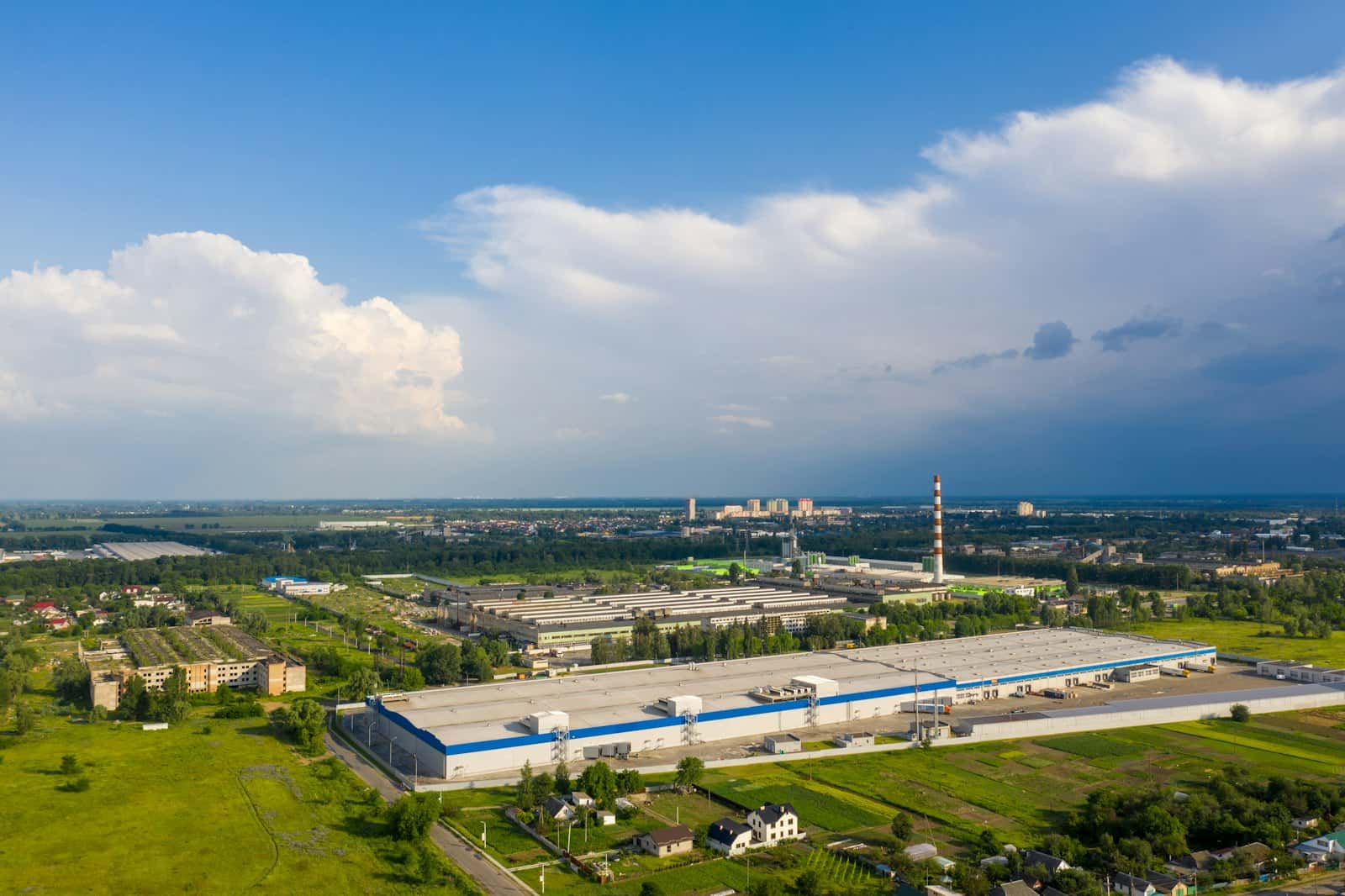 Aerial view of a large manufacturing plant with a white and blue facade, loading bays and green fields around it