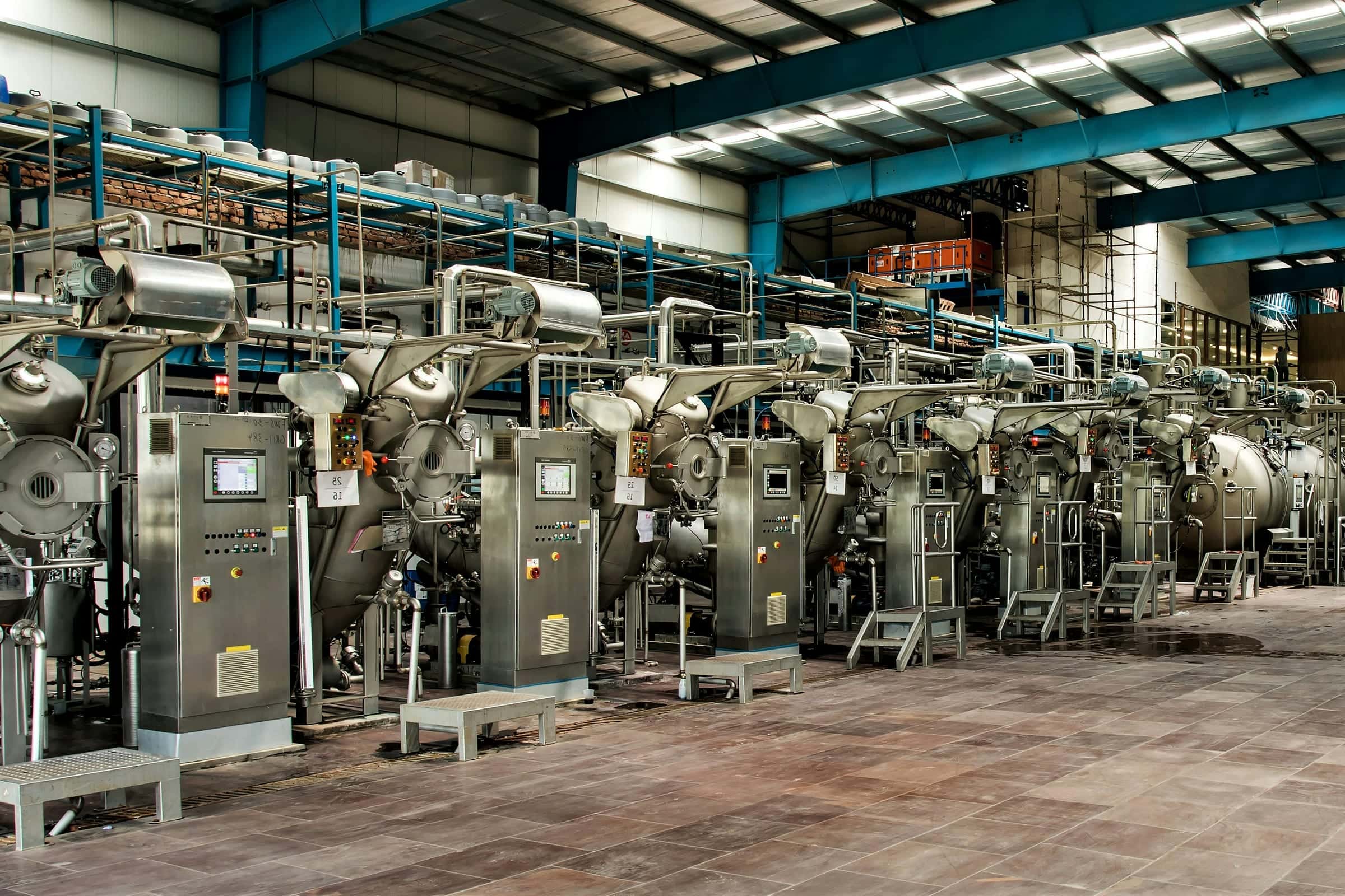 Long production hall with a row of stainless steel dyeing machines under a steel roof with skylights