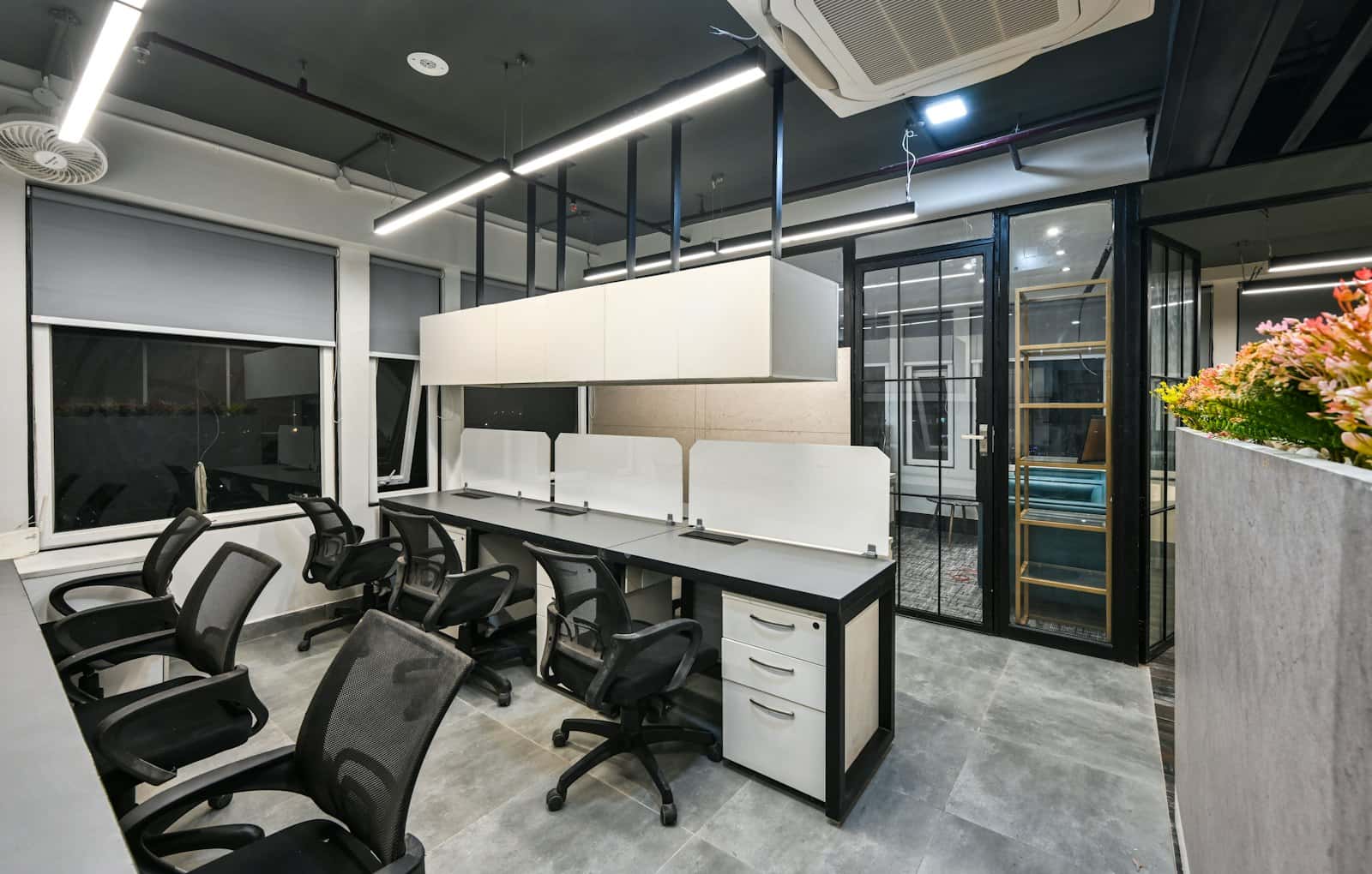 Compact office suite with a row of grey desks, white screens, mesh chairs and a black-framed glass cabin door
