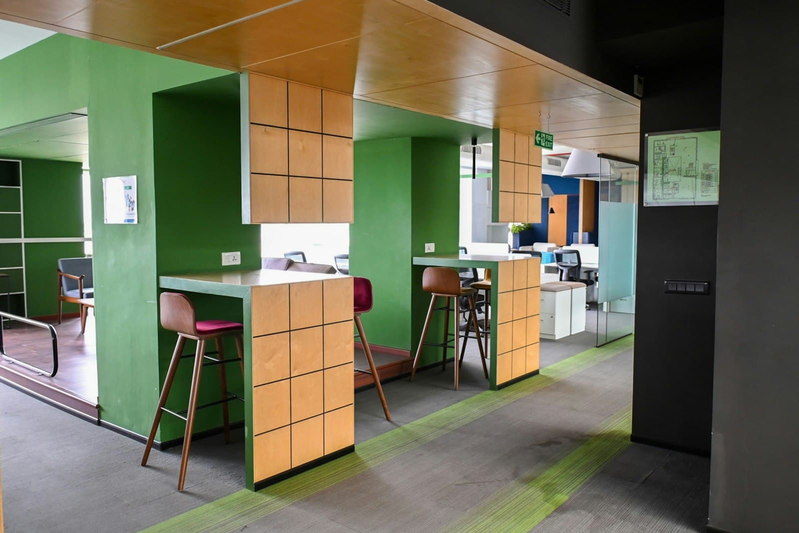 Collaboration nooks with green walls, timber counters and tall stools beside a carpeted walkway