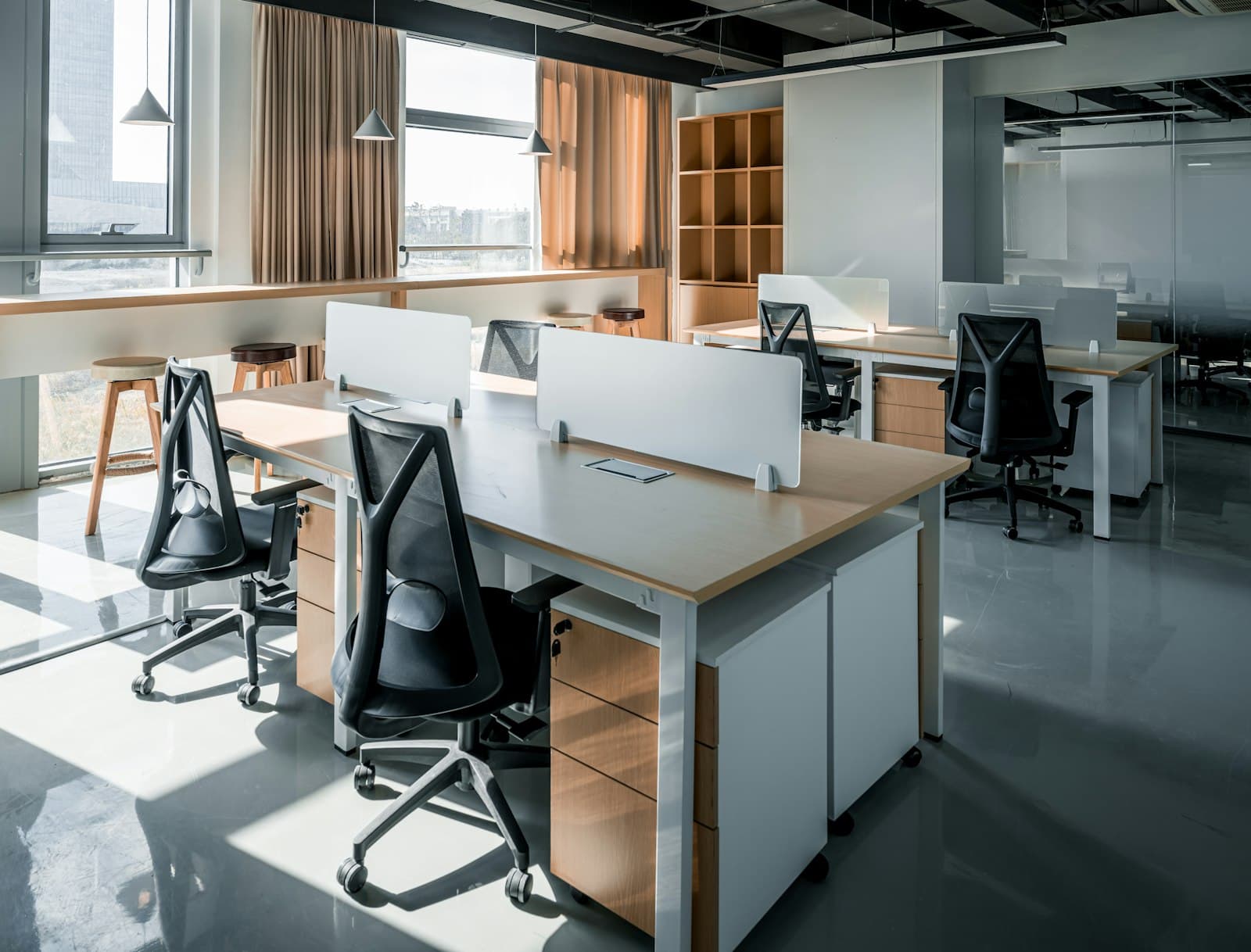Sunlit open-plan office with timber and white workstations, mesh chairs and a window counter with stools