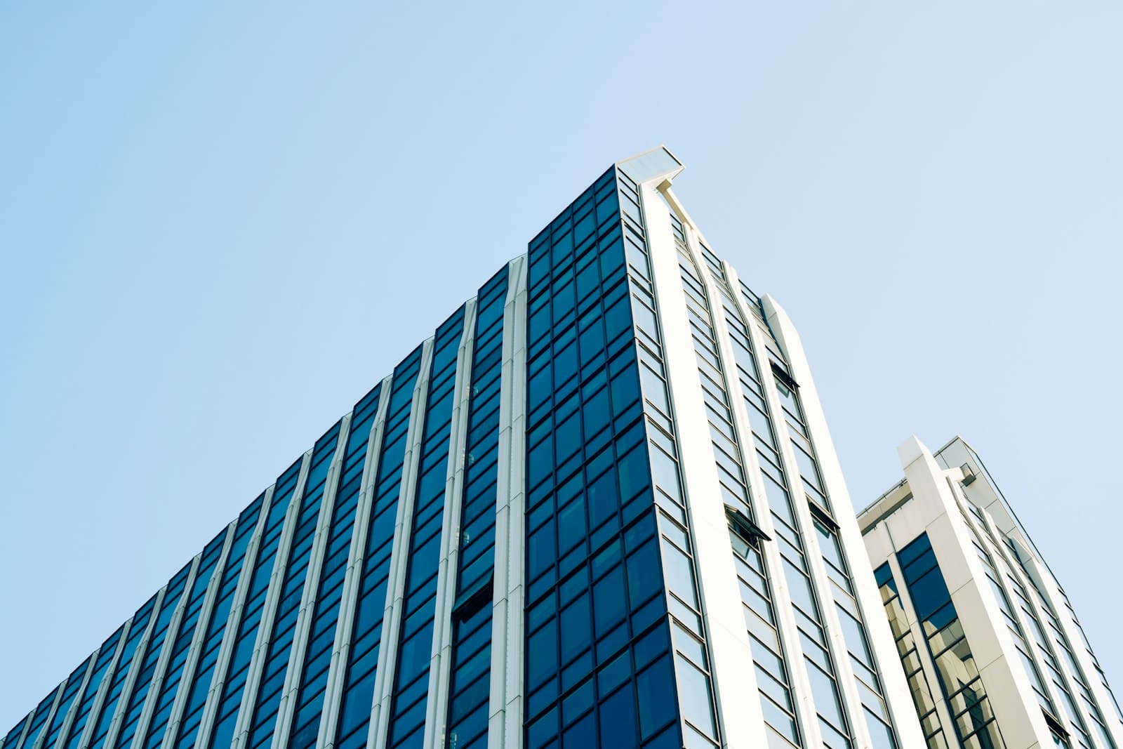 Low-angle view of a blue glass office tower with white vertical fins against a clear sky