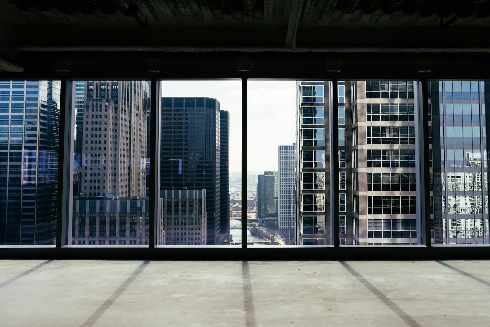 Bare concrete office floor with full-height windows framing neighbouring high-rise towers