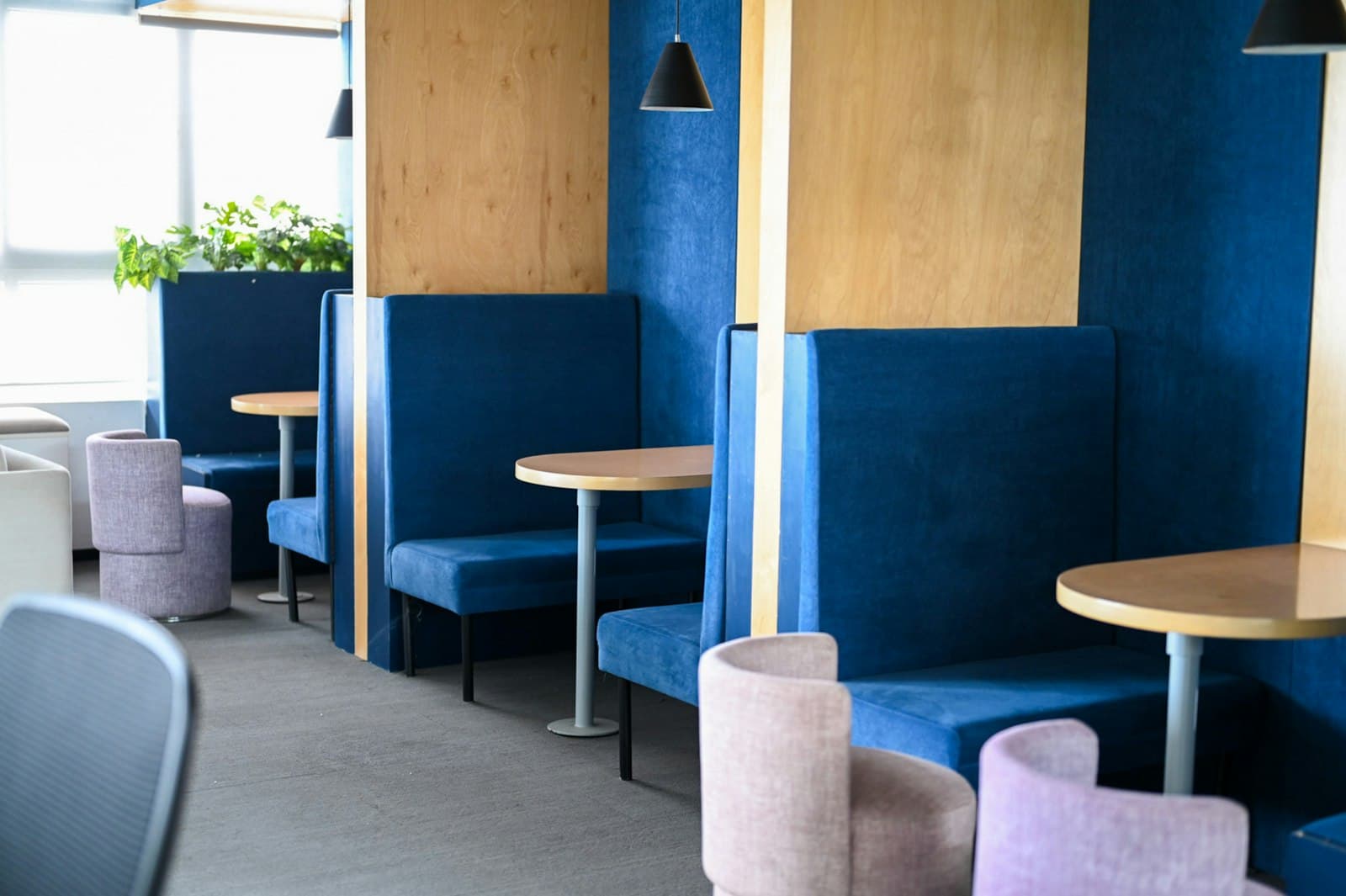 Breakout area of high-backed navy booths with round timber tables, lilac tub chairs and birch plywood panels