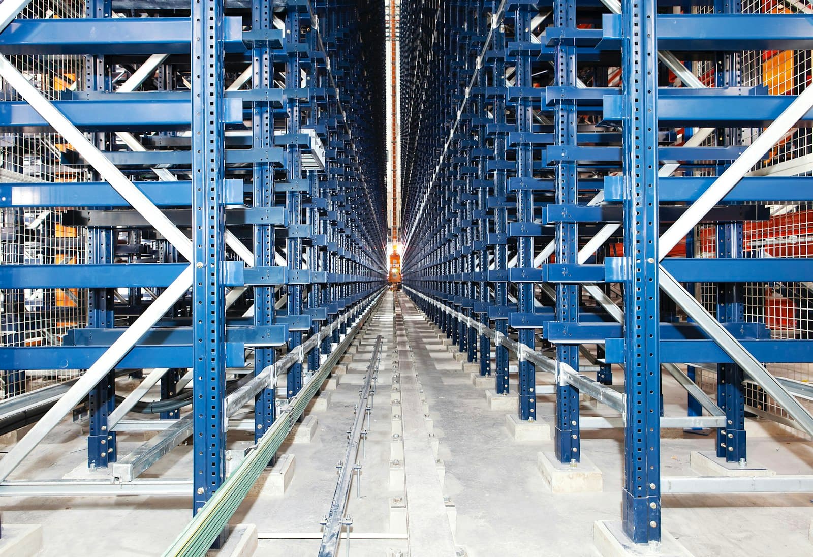 Long narrow aisle between towering blue steel storage racks with a guide rail running down the centre