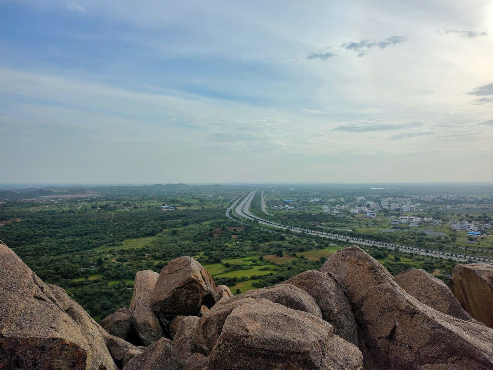 Granite boulders in the foreground overlooking a multi-lane ring road cutting through open scrubland