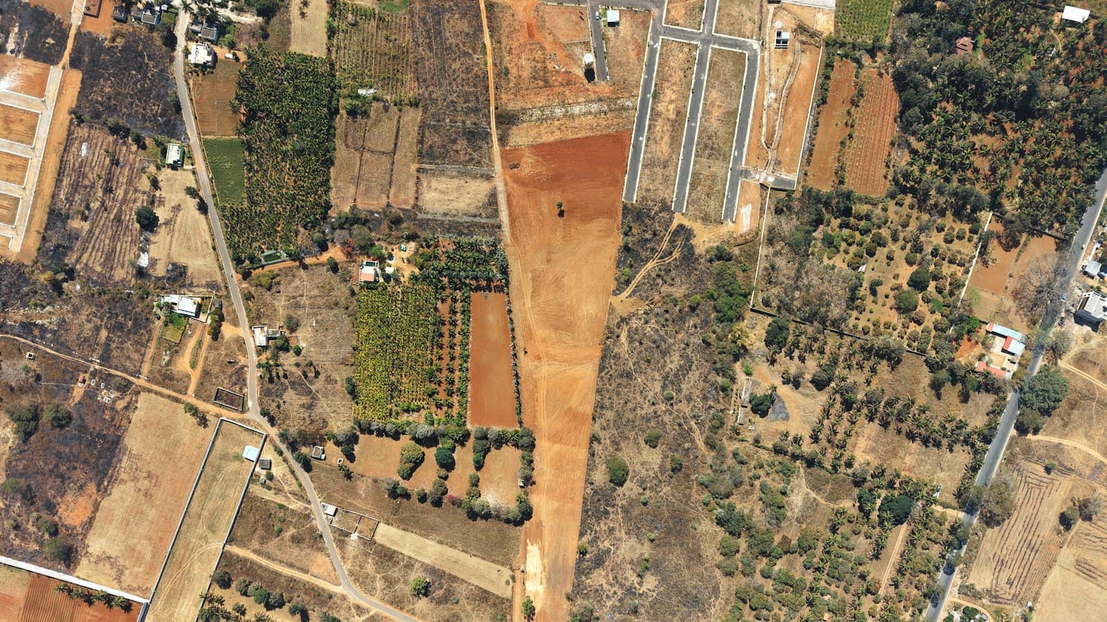 Overhead aerial of mixed land parcels, plantations and a newly laid plotted layout with internal roads