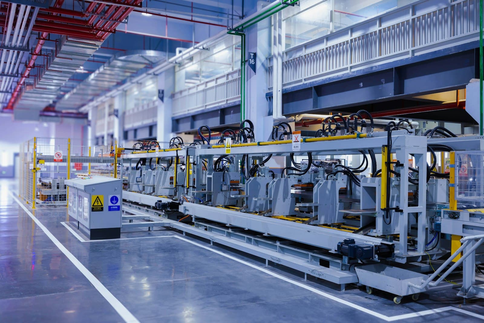 Automated production line on a clean, polished factory floor with safety fencing, a control cabinet and overhead ducts