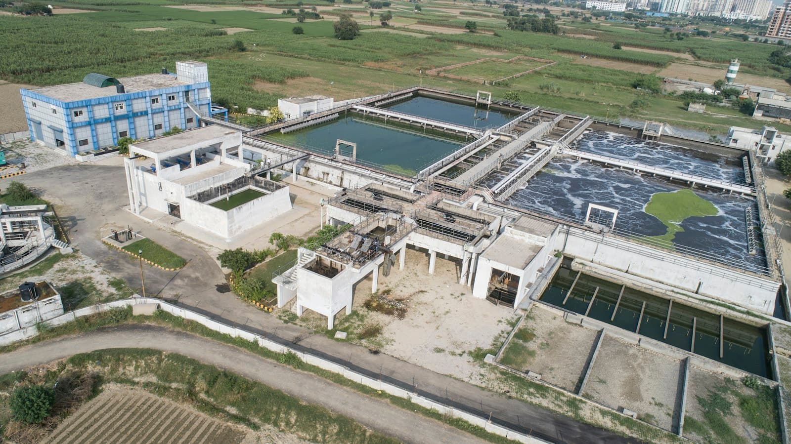 Aerial view of a wastewater treatment plant with settling tanks, aeration basins and a pump house beside farmland