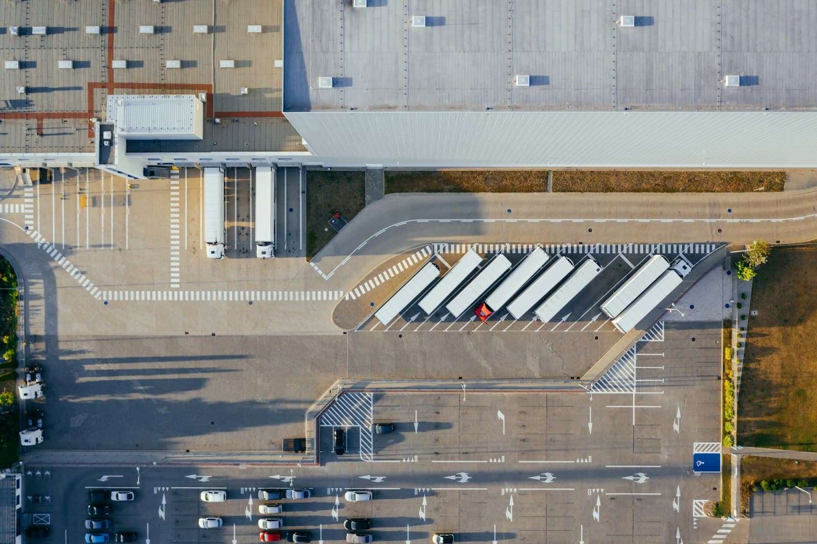 Overhead aerial of a large warehouse with trailers parked at its docks, a marked truck yard and a car park below