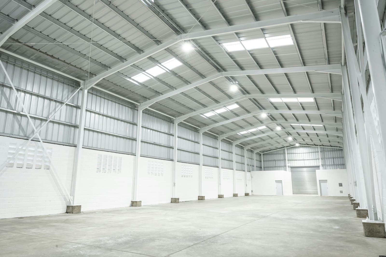 Empty light-industrial shed with white steel portal frames, roof skylights and a roller shutter at the far end
