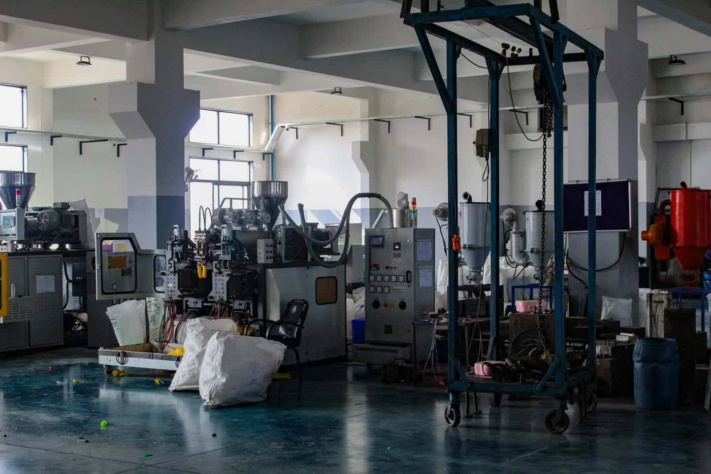 Factory floor with moulding machines, material hoppers and a steel hoist frame under a high ceiling lit by side windows