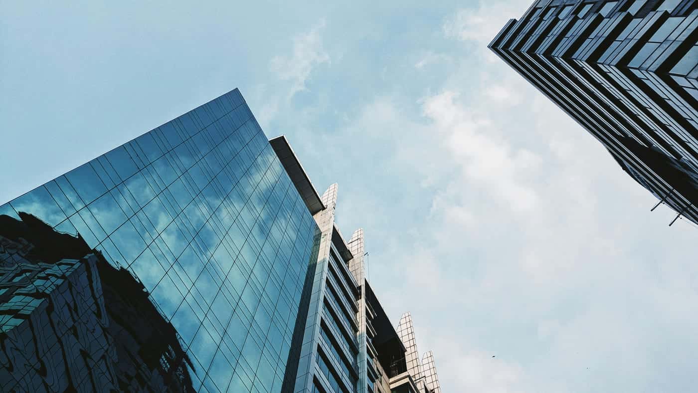 Glass-fronted office towers seen from below against a pale blue sky with light cloud