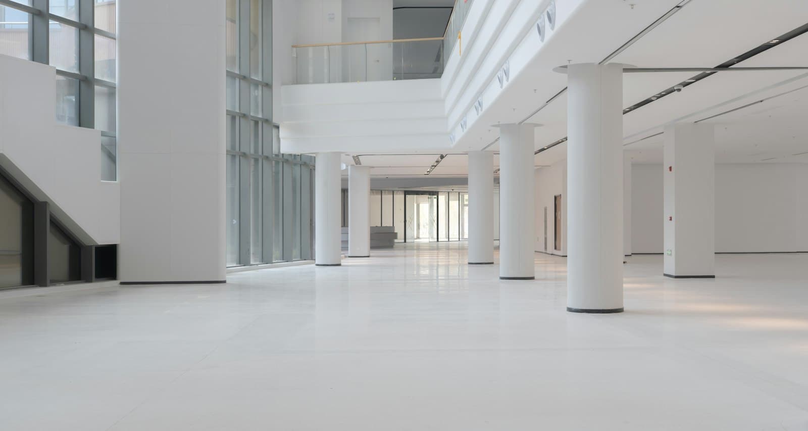 Bright unfurnished office floor with round white columns, glossy pale flooring and tall glazing