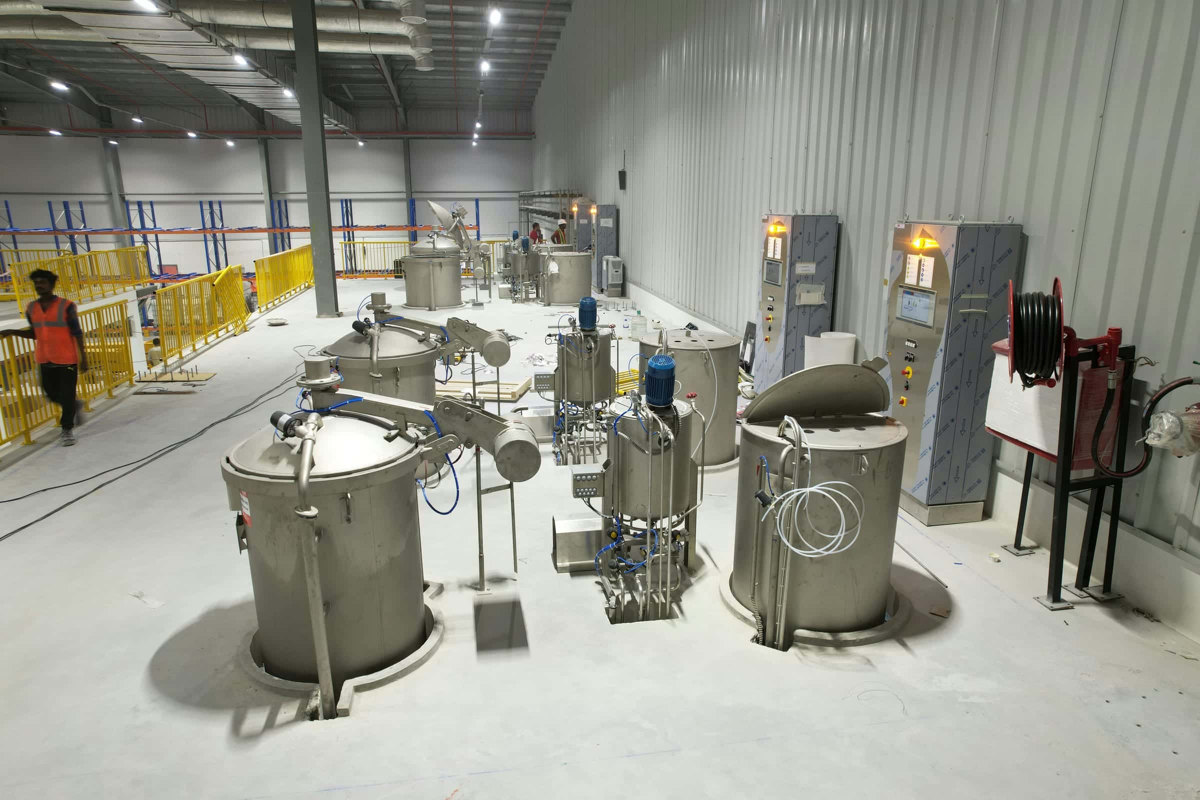 Clean, high-ceilinged factory hall with stainless steel yarn-dyeing vessels, control panels and a yellow safety rail